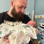 A father endearingly looks at his new baby in a hospital room.