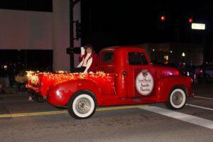 A photo of Annette Thurston, sitting in a vintage red truck, waving at the crowd during the Joplin Christmas Parade.